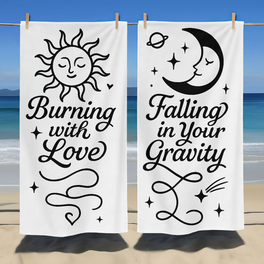 Holding up custom white beach towels with black sun and moon designs and romantic phrases, "Burning with Love" and "Falling in Your Gravity," on a sunny beach.