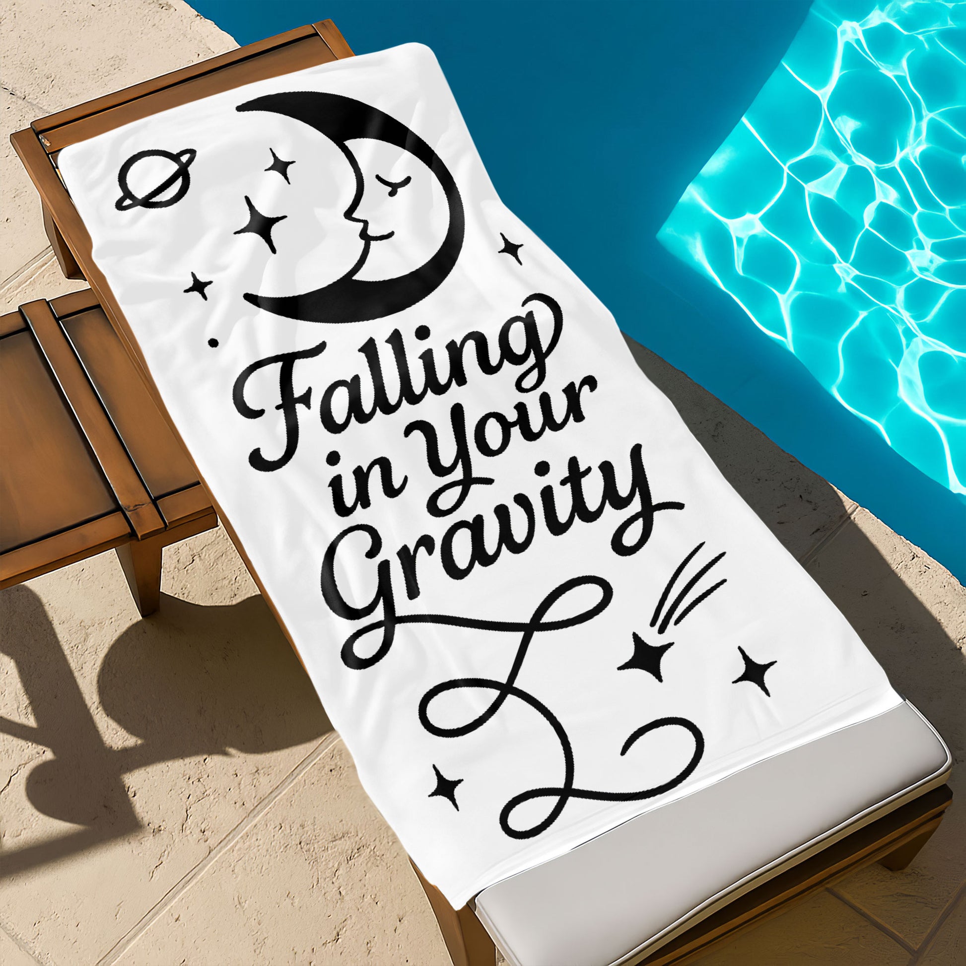 Two people holding up custom white beach towels with black sun and moon designs and romantic phrases, "Burning with Love" and "Falling in Your Gravity," on a sunny beach.