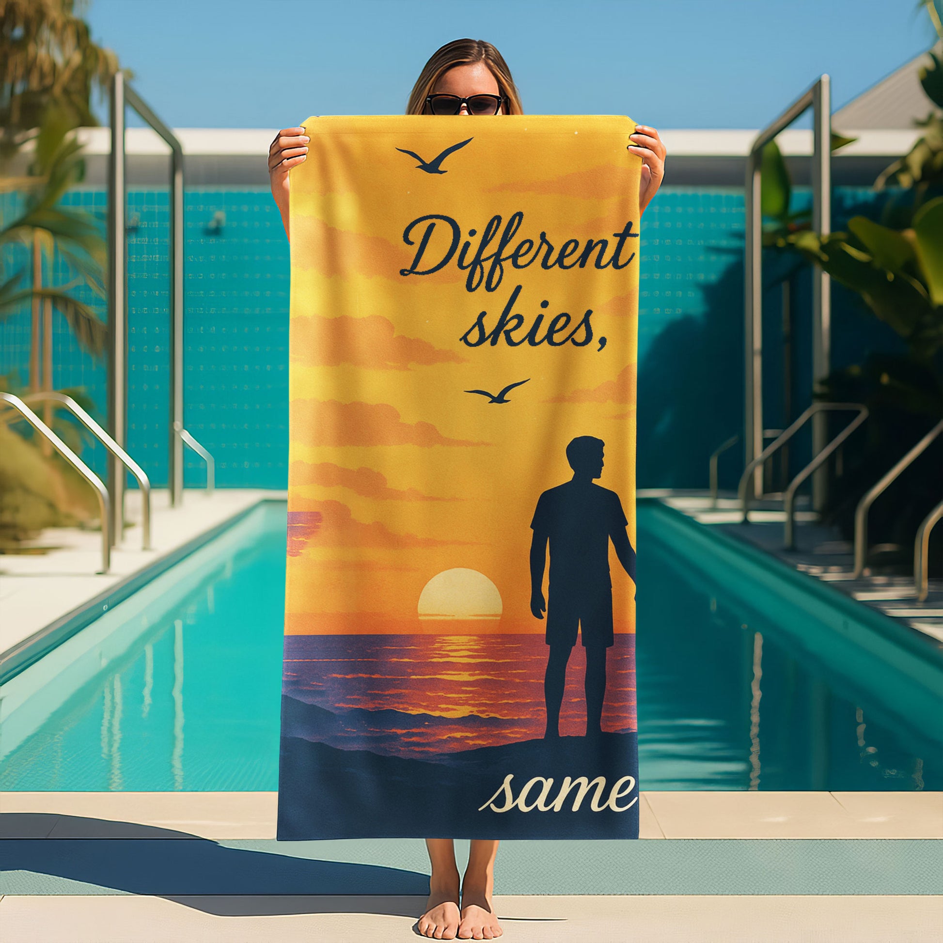 A man and a woman holding up custom beach towels on a beach. One towel shows a sunset scene with a male silhouette and text "Different skies, same love". The other shows a night sky scene with a female silhouette and text "love, same love".