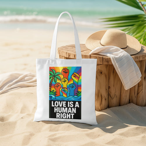 White tote bag with a design featuring multiple fists raised in the air, colored in the rainbow spectrum, against a background with a rainbow sky, palm trees, and ocean waves, with the text "LOVE IS A HUMAN RIGHT" in bold black letters.