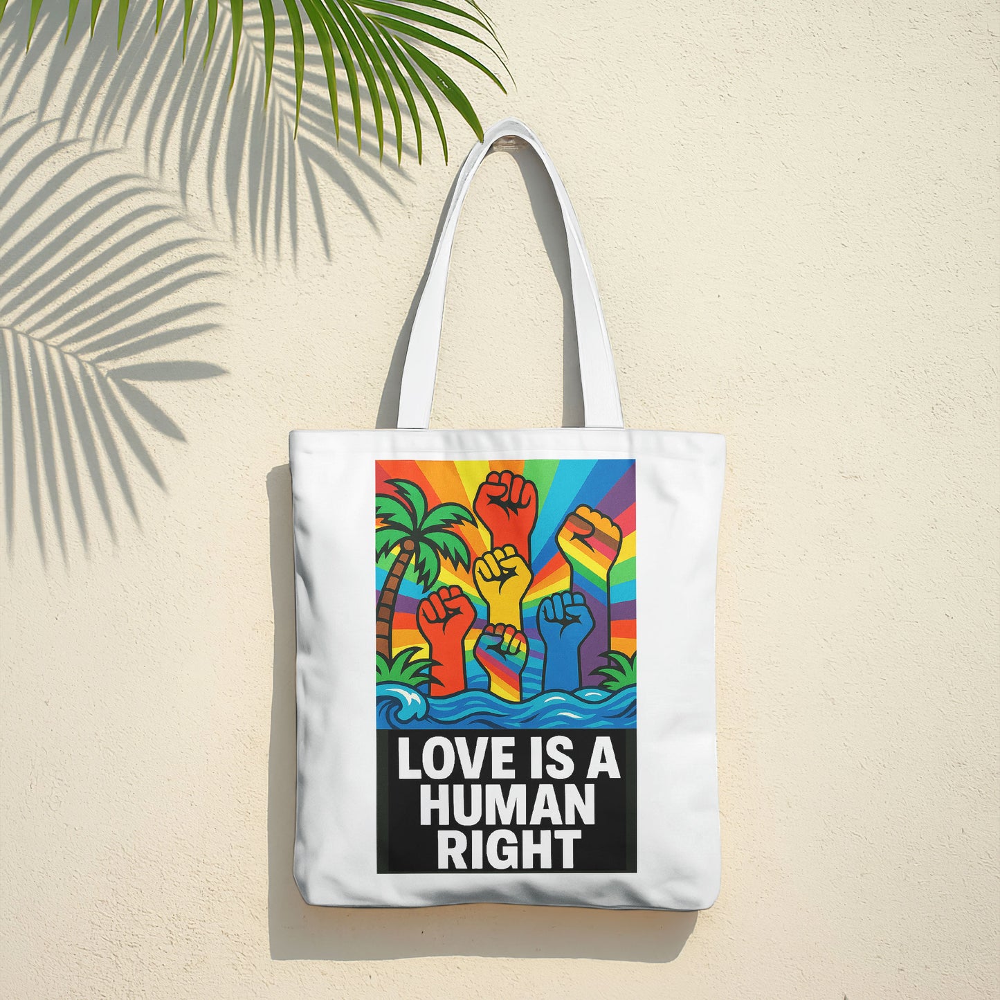 White tote bag with a design featuring multiple fists raised in the air, colored in the rainbow spectrum, against a background with a rainbow sky, palm trees, and ocean waves, with the text "LOVE IS A HUMAN RIGHT" in bold black letters