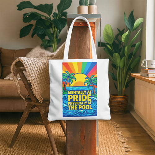 White tote bag with a design showing palm trees, a sunset with rainbow rays, ocean waves, and the text "MENTALLY AT PRIDE PHYSICALLY AT THE POOL