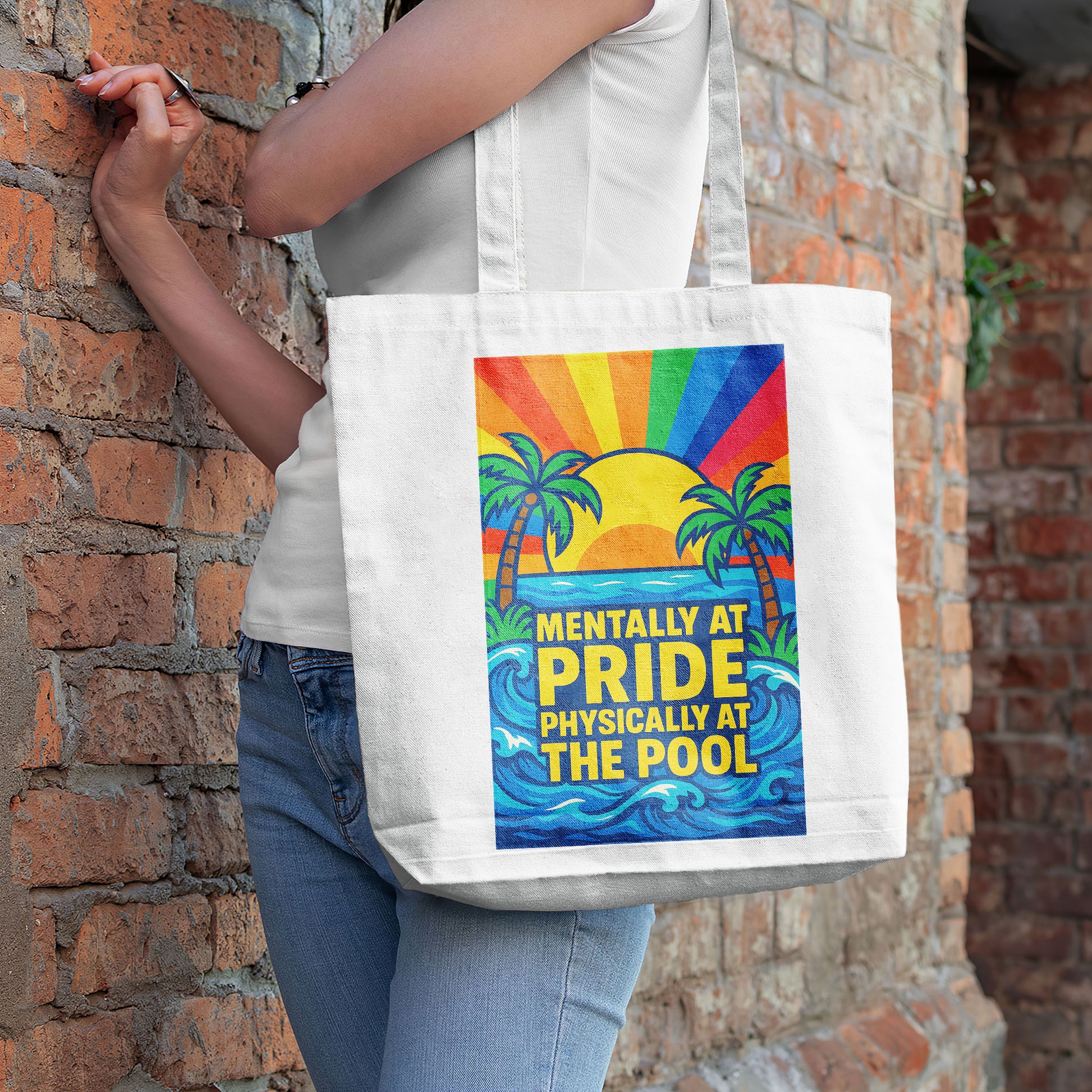 White tote bag with a design showing palm trees, a sunset with rainbow rays, ocean waves, and the text "MENTALLY AT PRIDE PHYSICALLY AT THE POOL