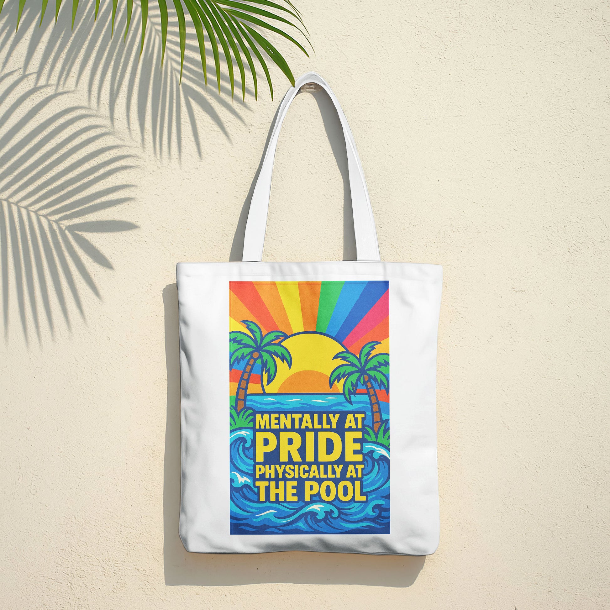 White tote bag with a design showing palm trees, a sunset with rainbow rays, ocean waves, and the text "MENTALLY AT PRIDE PHYSICALLY AT THE POOL