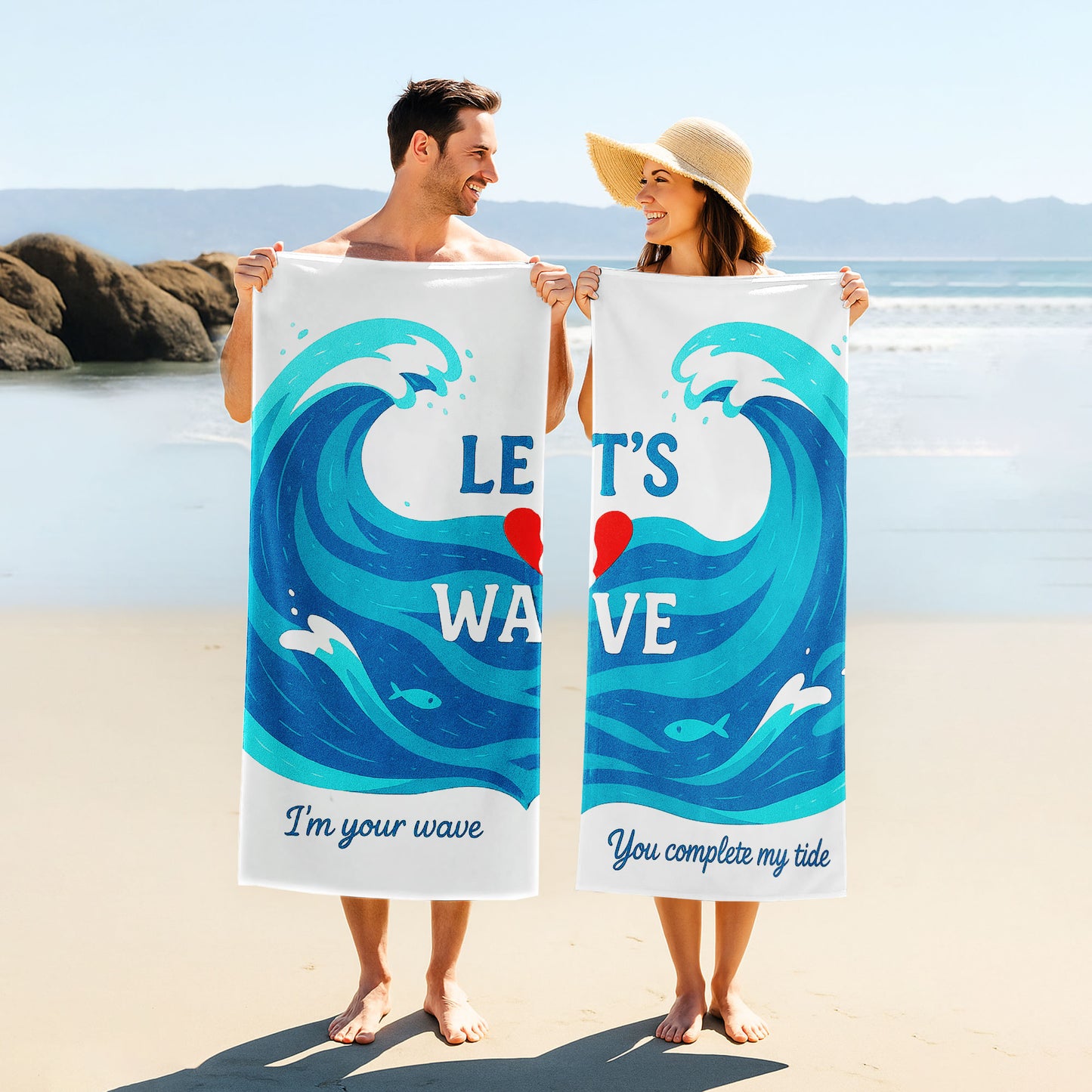 A couple holding up custom white beach towels with large blue wave designs and romantic phrases, "I'm your wave" and "You complete my tide," on a sunny beach.