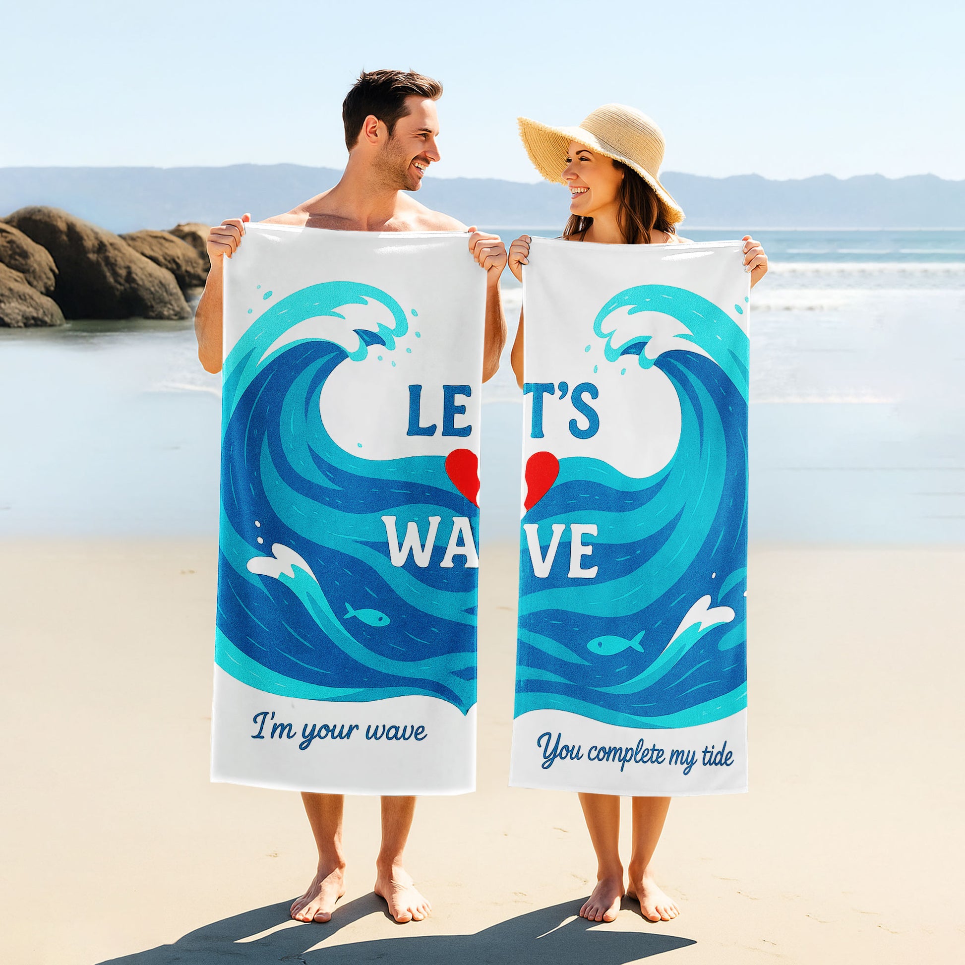 A couple holding up custom white beach towels with large blue wave designs and romantic phrases, "I'm your wave" and "You complete my tide," on a sunny beach.