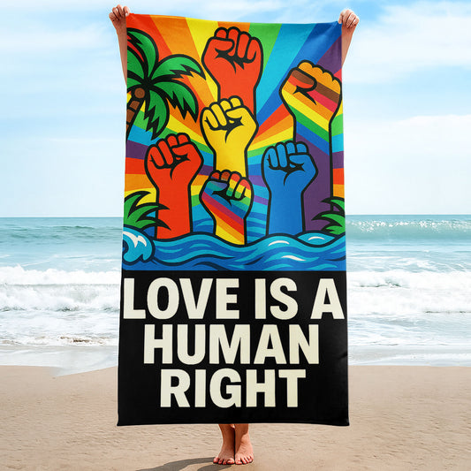 A person holding up a vibrant beach towel with a rainbow background featuring raised fists in various colors, tropical trees, and the bold text "LOVE IS A HUMAN RIGHT" on a black band at the bottom, on a sunny beach.