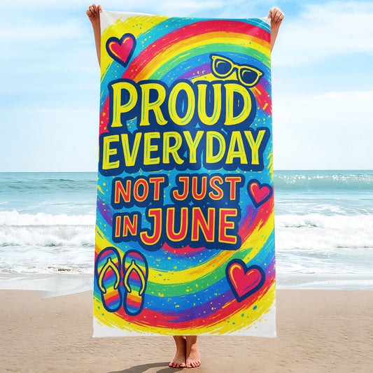 A person holding up a vibrant rainbow-colored beach towel with the bold yellow and pink text "PROUD EVERYDAY NOT JUST IN JUNE" along with hearts, sunglasses, and rainbow flip-flops, on a sunny beach.