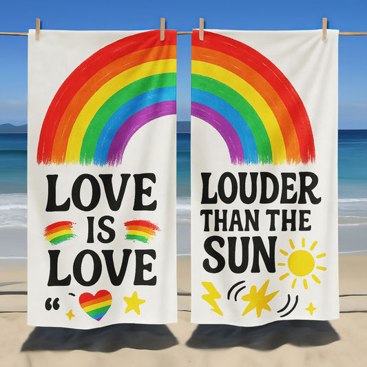 Two people holding up white beach towels with rainbow arches and text, one saying "LOVE IS LOVE" and the other "LOUDER THAN THE SUN," on a sandy beach under a clear sky.