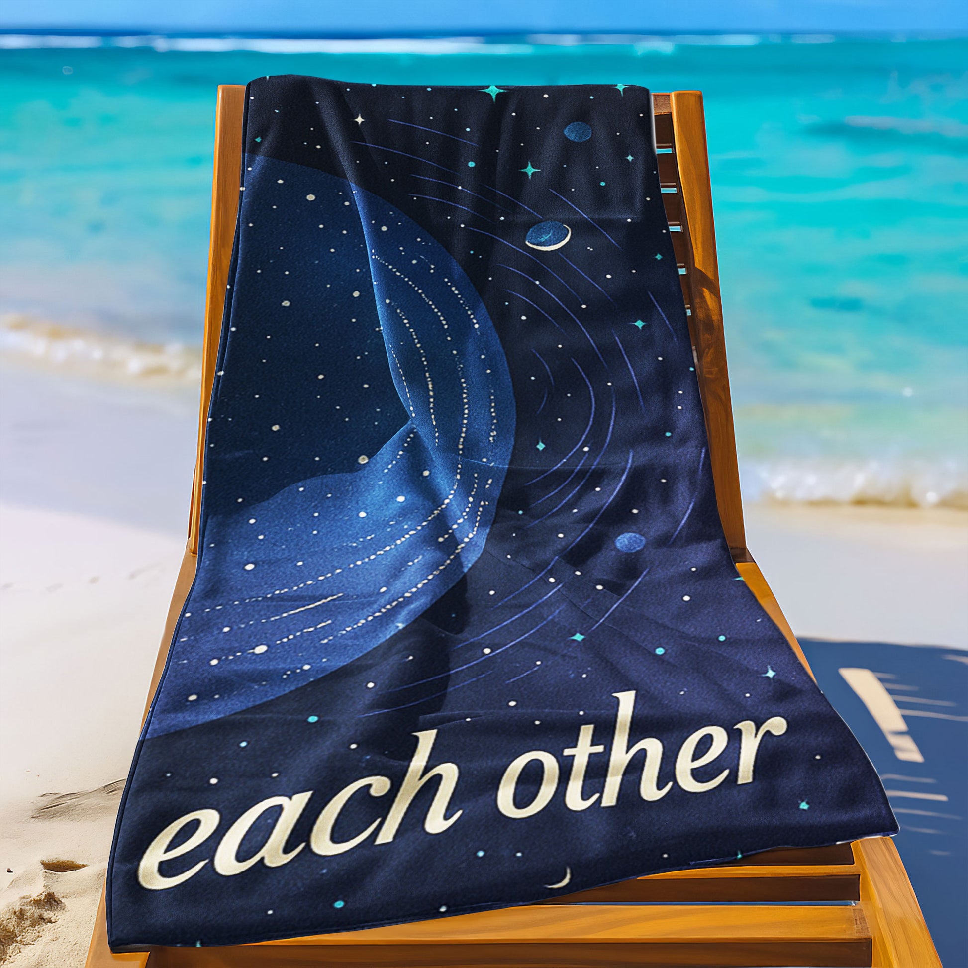  A man and a woman holding up custom beach towels on a beach. One towel shows a large golden planet with stars and "We orbit each other". The other shows a blue planet with orbits and stars, also part of "We orbit each other".