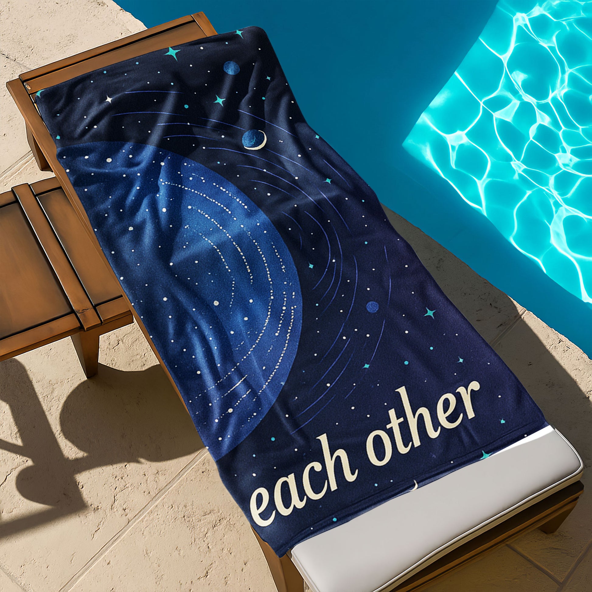  A man and a woman holding up custom beach towels on a beach. One towel shows a large golden planet with stars and "We orbit each other". The other shows a blue planet with orbits and stars, also part of "We orbit each other".